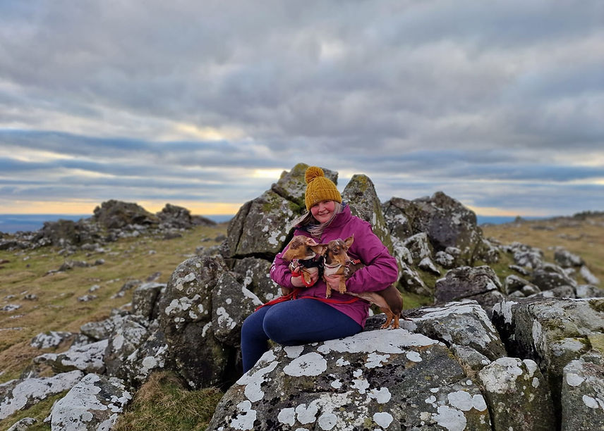 Melanie hugging her two dachshunds Happy and Joy on a Dartmoor tor at golden hour